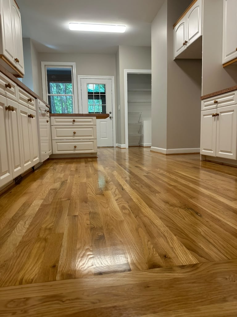 Freshly refinished hardwood flooring in a bright white kitchen